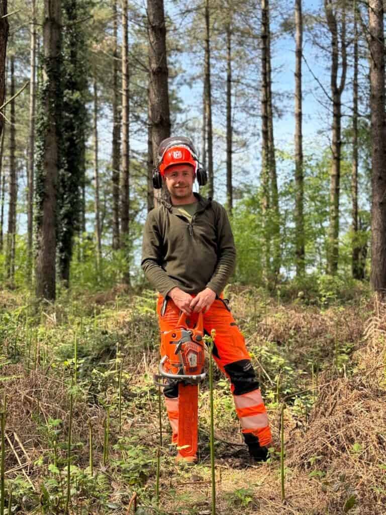 A forester stands in a forest with a chainsaw.