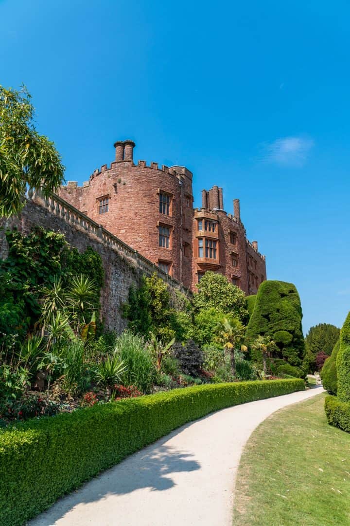 Picturesque path leading to Powis Castle in Wales with lush gardens and blue sky.